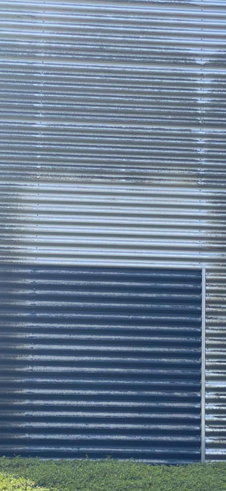 Gegolfd metalen gebouw met groene planten ervoor.