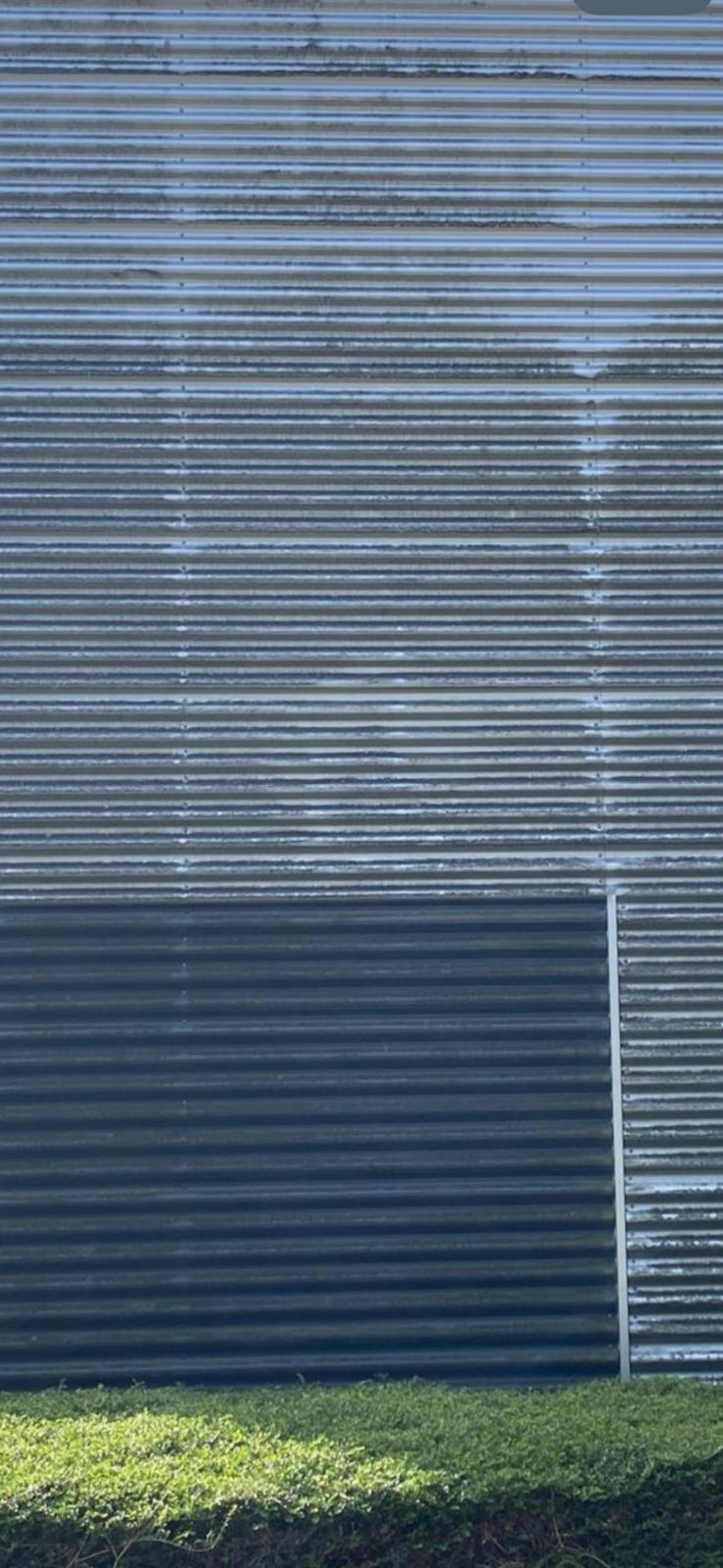 Golvend metalen muur met groene struiken ervoor.