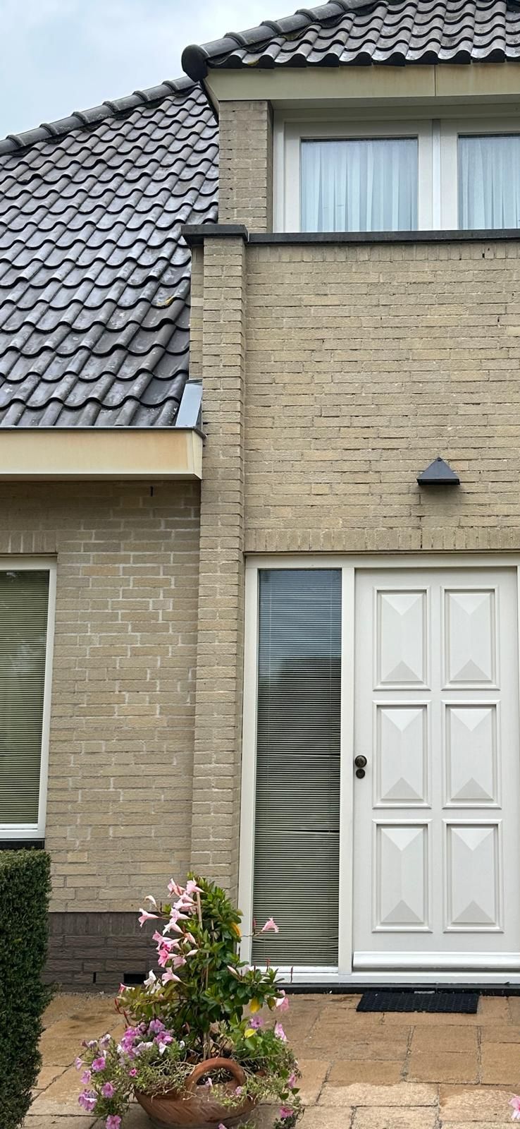 Witte voordeur van een bakstenen huis met bloemen