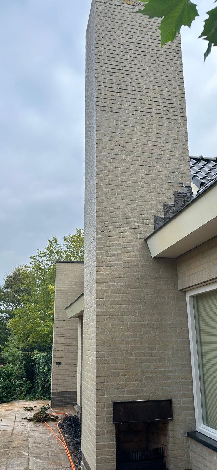 Bakstenen schoorsteen naast huis met tuin en tegels.