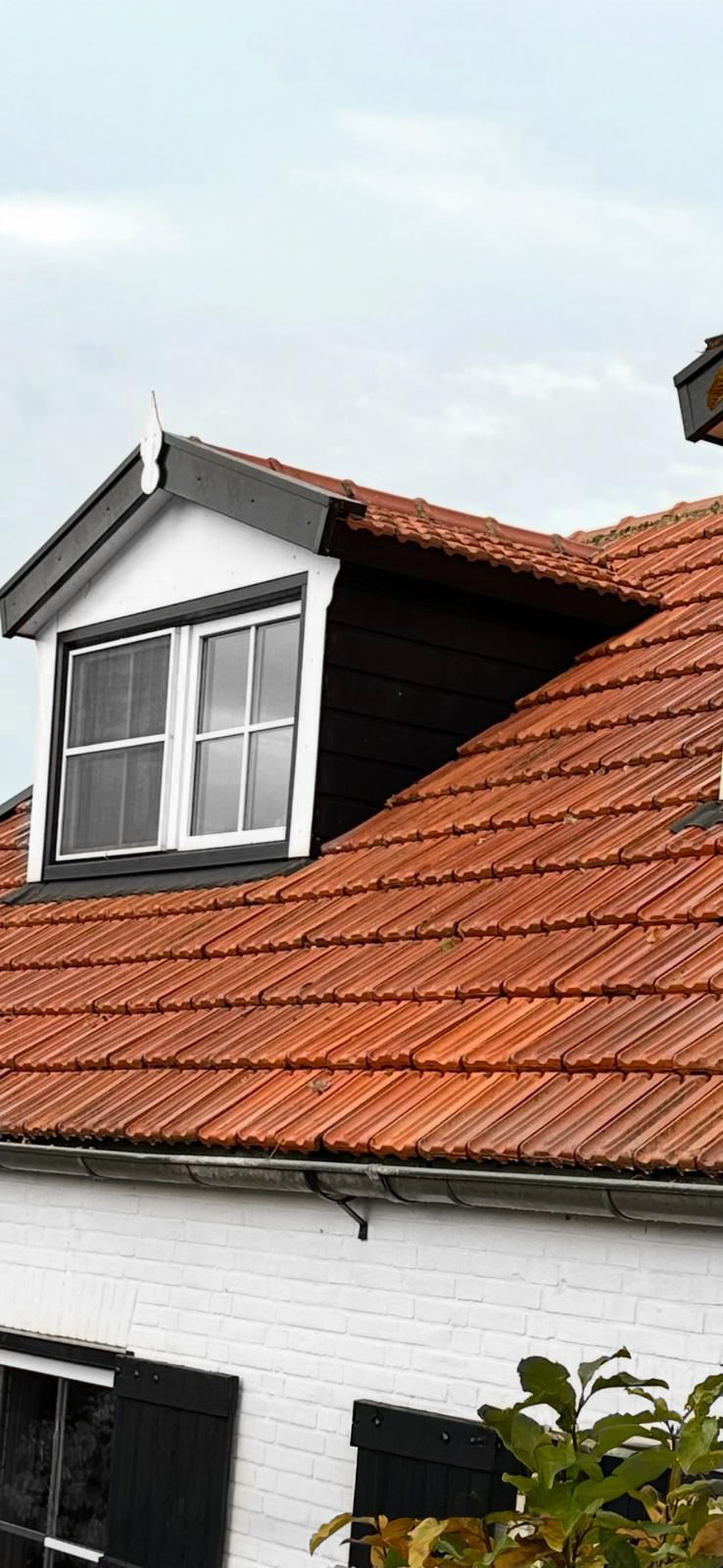 Rood pannendak met dakkapel op wit huis.